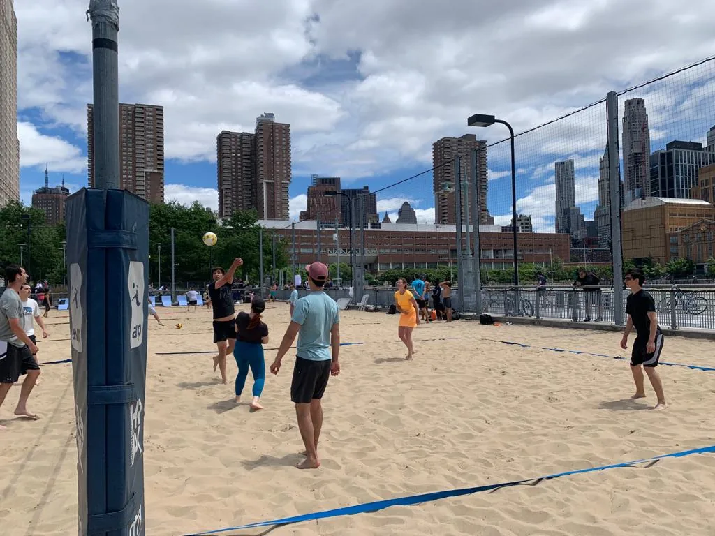 A beach volleyball game with the New York skyline behind it