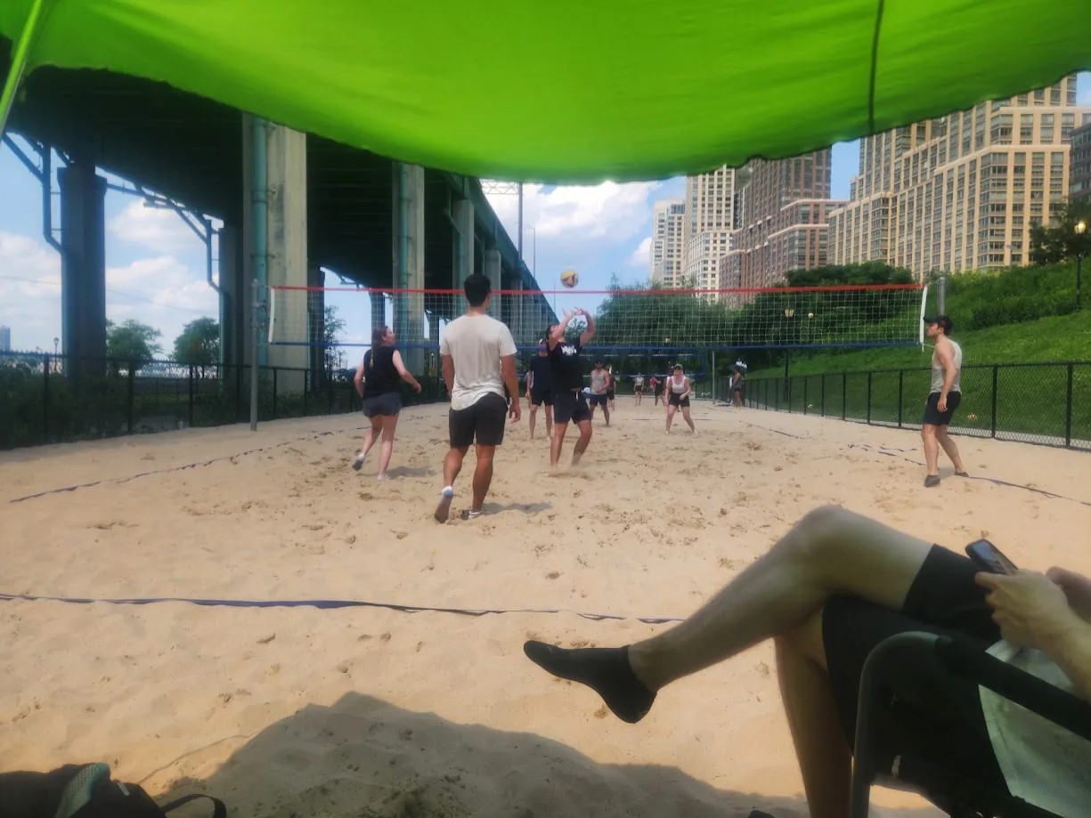 A volleyball game on a sand court beneath an elevated roadway