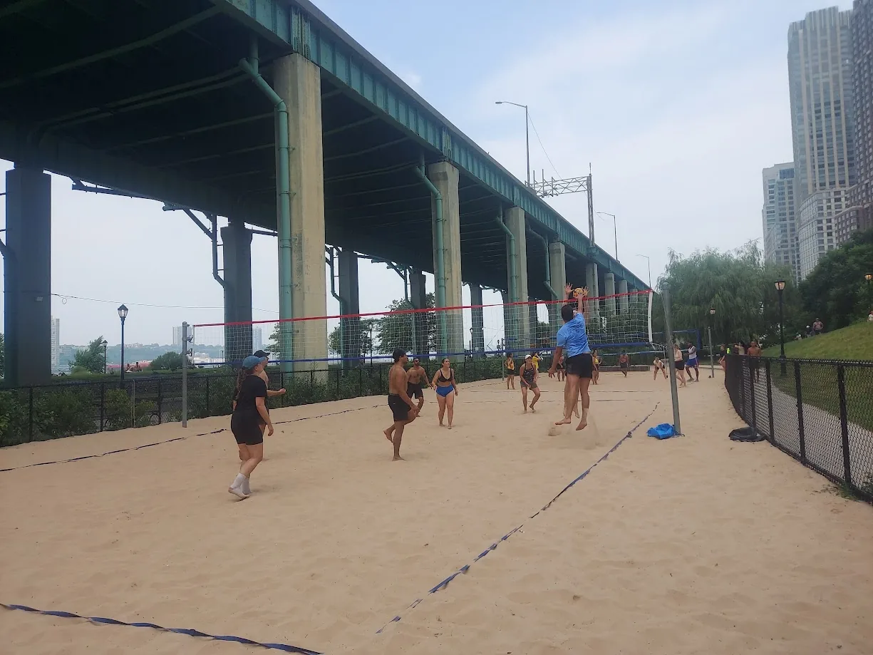 Players competing on a sand volleyball court beneath an elevated roadway
