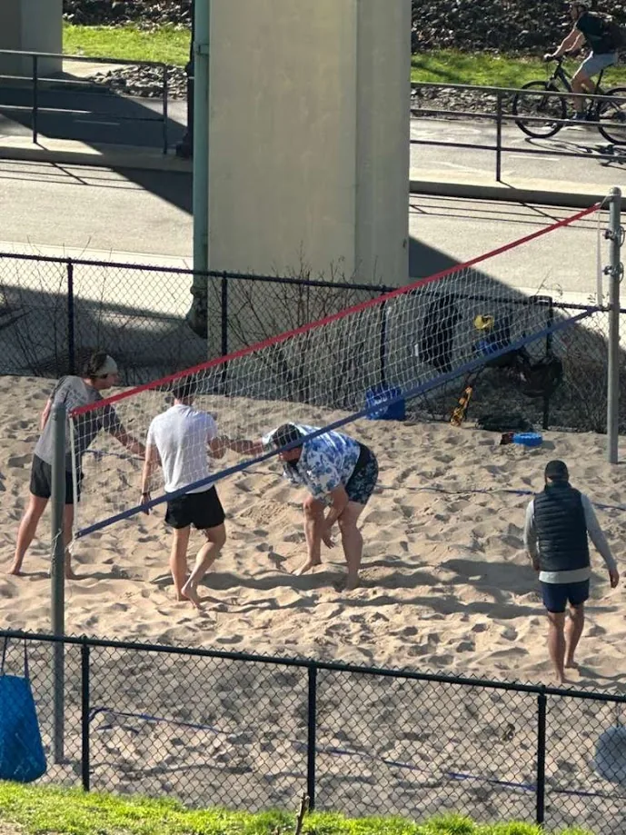 Players adjusting a sagging volleyball net on a sand court