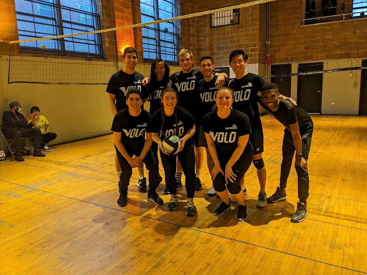 A volleyball team posing together on an indoor court in matching black Volo shirts